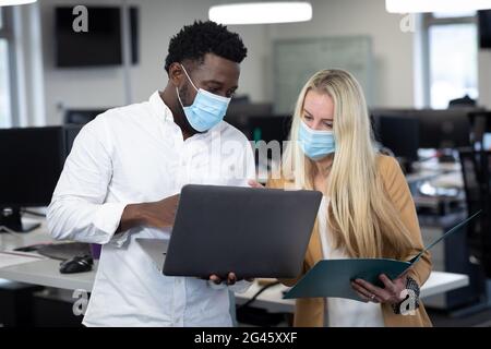 Uomo d'affari e uomo d'affari che indossano maschere di faccia che lavorano insieme a moderno ufficio Foto Stock