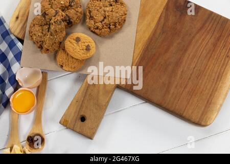 Vista di biscotti, cucchiai di frutta secca e uova su superficie di legno bianco con tovaglia Foto Stock