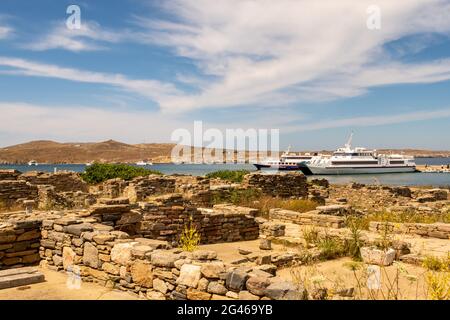Vista di una baia sull'isola di Delos, Grecia, con navi turistiche da Mykonos ancorate e antiche rovine e colonne della città in primo piano. Foto Stock