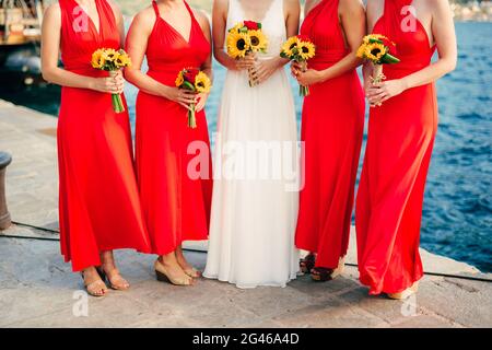 Bridesmaids in abiti rossi, in mani mazzi di girasoli. Mer Foto Stock