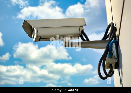 Si tratta di una telecamera di sicurezza appesa alla parete di un edificio contro un cielo blu con nuvole in una giornata estiva. Foto Stock