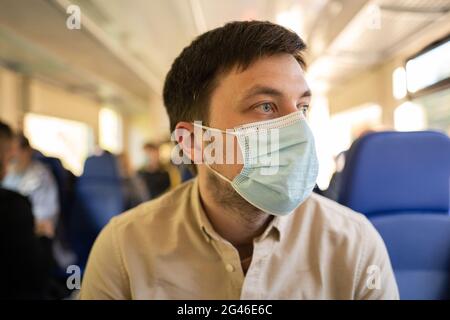 Uomo che viaggia in treno indossando una maschera facciale. Distanza sociale quando si viaggia in treno durante la pandemia di Covid-19. Il maschio commuta a. Foto Stock