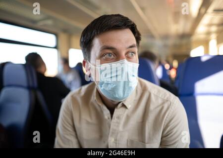 Uomo che viaggia in treno indossando una maschera facciale. Distanza sociale quando si viaggia in treno durante la pandemia di Covid-19. Il maschio commuta a. Foto Stock