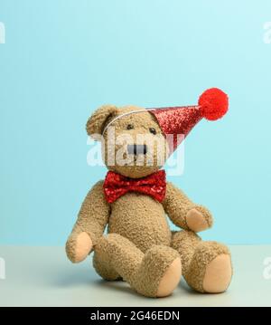 Orsacchiotto marrone in un cappuccio rosso si siede su uno sfondo blu, Foto Stock