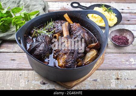 Stinco di agnello brasato tradizionale di stile moderno e cotto lentamente in salsa di vino rosso con scalogni e purè di patate offerto come vista dall'alto Foto Stock