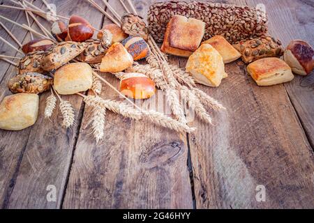 Ampia selezione di panini appena sfornati su sfondo rustico in legno con un fascio di grano Foto Stock