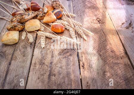 Ampia selezione di panini appena sfornati su sfondo rustico in legno con un fascio di grano Foto Stock