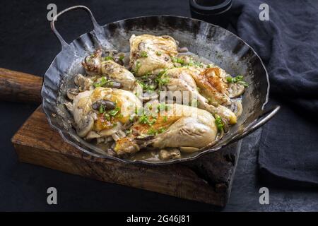 Ali di pollo fritte tradizionali e gambe con funghi in salsa di vino serviti da primo piano in una padella rustica in ferro battuto Foto Stock