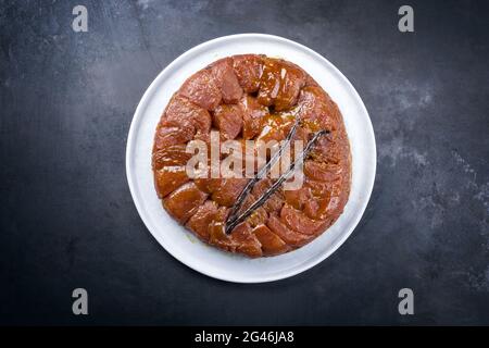 Tradizionale tatin francese con mele e vaniglia offerto come vista dall'alto su un moderno piatto di design nordico con backgroun rustico Foto Stock