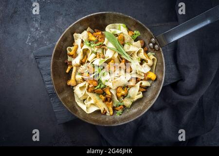 Tagliatelle tradizionali fritte con galletti con funghi offerti come vista dall'alto in una rustica padella di ferro Foto Stock