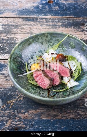 Tagliata di manzo italiana in stile moderno con bistecca di sidro affettato e insalata di agnello stagionato e servita da primo piano in una ceramica di design Foto Stock
