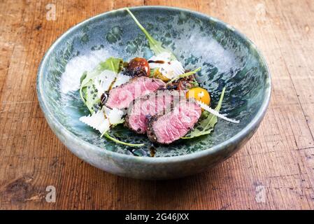 Tagliata di manzo italiana in stile moderno con bistecca di sidro affettato e insalata di agnello stagionato e servita da primo piano in una ceramica di design Foto Stock