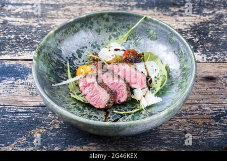Tagliata di manzo italiana in stile moderno con bistecca di sidro affettato e insalata di agnello stagionato e servita da primo piano in una ceramica di design Foto Stock