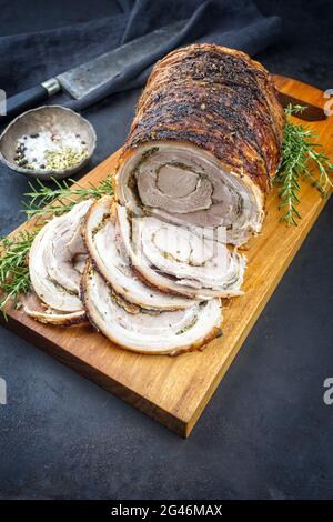 Carne di maiale tradizionale italiana Porchetta arrotolata tagliata a fette e come pezzo con crosta offerta da primo piano su un legno dal design moderno Foto Stock