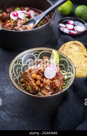 Stile moderno tradizionale pozole rojo messicano cotto lento con tortilla servito da primo piano in una ciotola di design su una tavola rustica Foto Stock