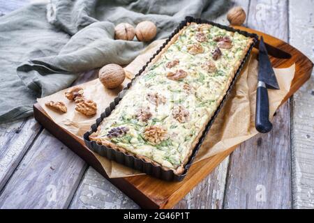 Tradizionale tarte francese di spinaci di noce d'autunno servito da primo piano in una forma di supporto su un moderno bordo di legno di design Foto Stock