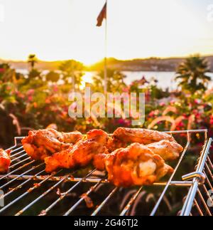 La cottura di spiedini di pollo alla griglia nel giardino al tramonto Foto Stock