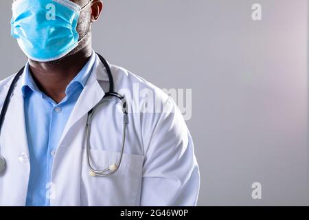 Sezione centrale del medico africano americano maschio che indossa la maschera facciale su sfondo grigio Foto Stock