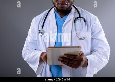 Metà della sezione del medico africano americano maschio che usa la compressa digitale su sfondo grigio Foto Stock