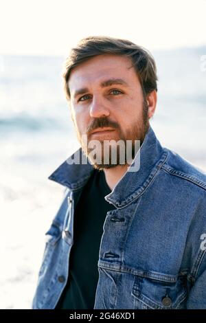 Ritratto di un uomo pensivo in una giacca in denim sullo sfondo del mare. Primo piano Foto Stock