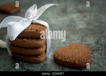 Vista laterale di una pila di biscotti al cioccolato a forma di cuore con un nastro festivo. Sfondo festivo Foto Stock