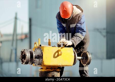 Un uomo in abiti da lavoro e un elmetto lavora con attrezzature a gas all'aperto in inverno. Riparazione della gru lineare Foto Stock