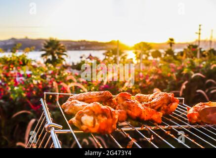 La cottura di spiedini di pollo alla griglia nel giardino al tramonto Foto Stock