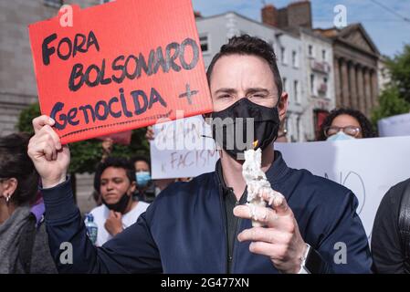 Dublino, Irlanda. 19 giugno 2021. Un manifestante tiene una candela accesa e un cartello durante la dimostrazione.i manifestanti si sono riuniti alla spire per manifestare contro il presidente brasiliano Jair Bolsonaro. I manifestanti hanno chiesto una migliore distribuzione dei vaccini Covid-19 in Brasile, così come un'azione sul recente aumento della fame nel paese e sull'impeachment di Bolsonaro. Credit: SOPA Images Limited/Alamy Live News Foto Stock