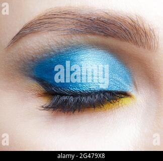 Occhio femminile chiuso con occhi fumosi blu ombre e liner giallo. Foto Stock