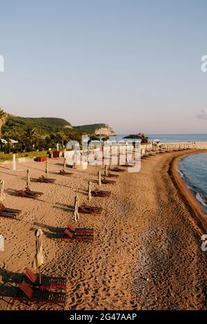 Budva, Montenegro - 12 luglio 2020: Lettini in legno con ombrelloni su una spiaggia di sabbia in Montenegro, vicino all'isola di Sveti Foto Stock