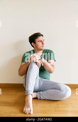 L'uomo in pantaloni e una t-shirt si siede sul pavimento appoggiandosi a una parete Foto Stock