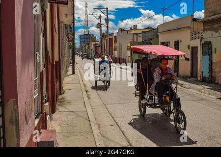 Bici-taxi in auto lungo una strada secondaria a Holguin, Cuba Foto Stock