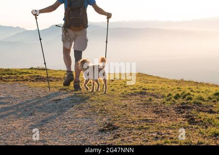 Escursionista con cane e zaino con bastoni da passeggio su una montagna al tramonto. Foto Stock
