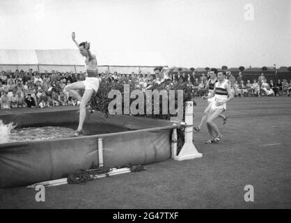 1954, storico, fuori su una pista d'erba, concorrenti maschi affrontare un salto d'acqua nel Mens steeplechase in una giornata di sport del servizio pubblico, Inghilterra, Regno Unito. Foto Stock