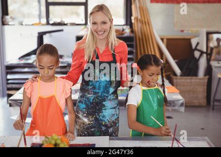 Insegnante sorridente in piedi con bambini in classe di disegno Foto Stock