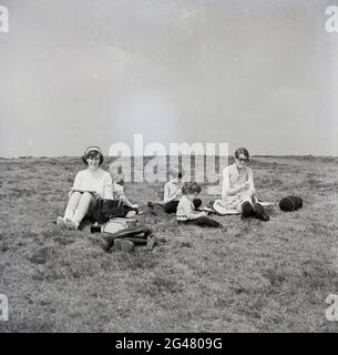 1960s, storico, due madri con bambini seduti su una collina con uno spuntino e un riposo dopo una passeggiata, Shropshire, Inghilterra, Regno Unito. Un altopiano naturale, le colline Shropshire è un'area di straordinaria bellezza naturale e popolare luogo per le vacanze in famiglia. Foto Stock