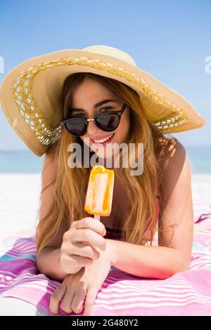 Ritratto di donna che tiene il papsicle mentre si rilassa in spiaggia Foto Stock