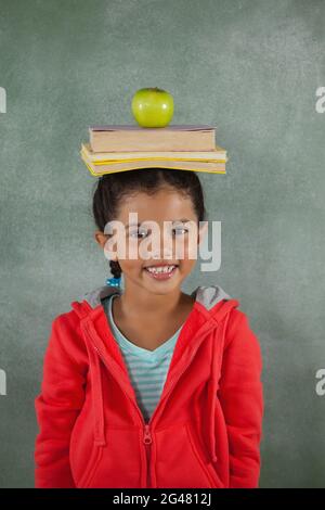 Giovane ragazza che bilancia libri e mela sulla testa Foto Stock