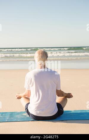 Vista posteriore del senior uomo fare yoga in spiaggia Foto Stock