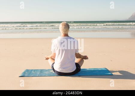 Vista posteriore del senior uomo meditando a beach Foto Stock