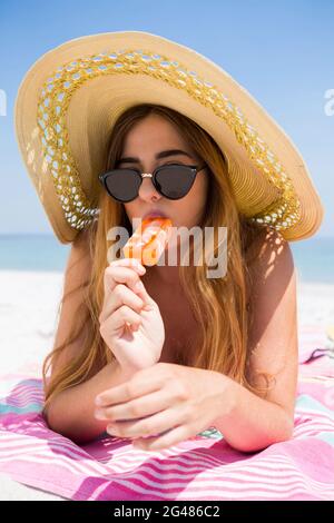 Ritratto di donna che mangia il papsicolo mentre si rilassa in spiaggia Foto Stock