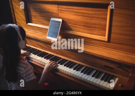 Vista ad alto angolo della ragazza che indossa le cuffie mentre si pratica il pianoforte in classe Foto Stock