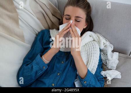 Vista ad alto angolo della donna che sfrega il naso mentre si sdraiava sul divano Foto Stock