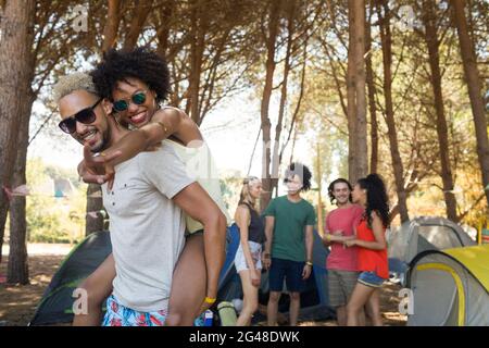 Uomo piggybacking donna con amici in background Foto Stock