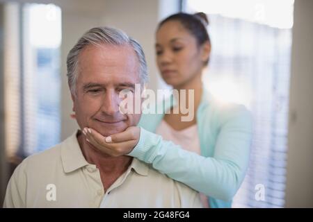 Giovane terapista femminile che dà massaggio al collo a paziente anziano Foto Stock