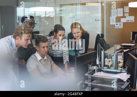 Uomo d'affari che discute con i colleghi mentre lavora sul computer visto attraverso il vetro Foto Stock