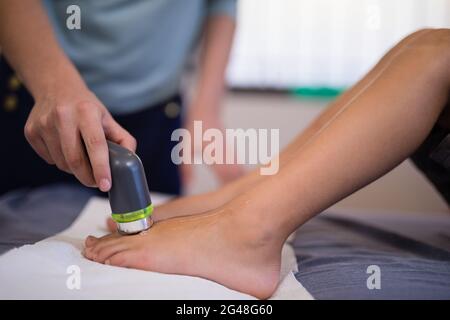Sezione bassa del ragazzo che riceve ecografia sui piedi da terapeuta femminile Foto Stock