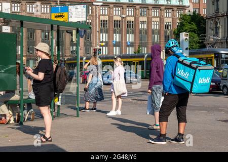 Wolt corriere per la consegna di cibo con zaino termico in attesa di un autobus a Helsinki, Finlandia Foto Stock