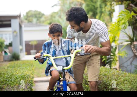 Uomo che assiste il figlio in bicicletta Foto Stock