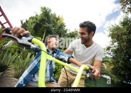 Felice padre che assiste il figlio mentre si guida in bicicletta Foto Stock